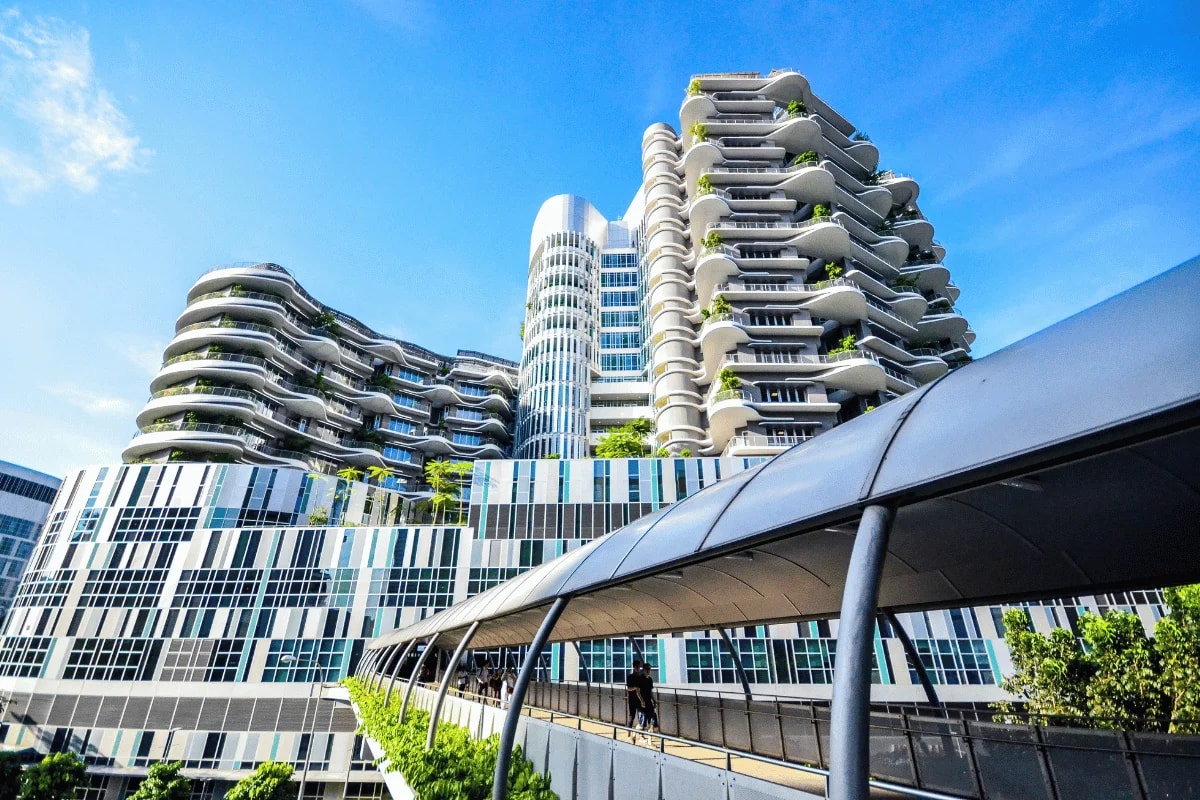 A futuristic building with curved balconies and abundant greenery, viewed under a bright blue sky.