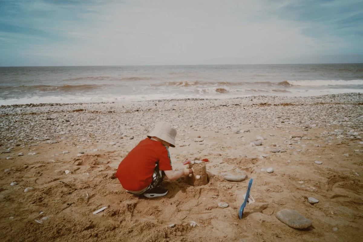 Child building a sandcastle on a sunny beach.