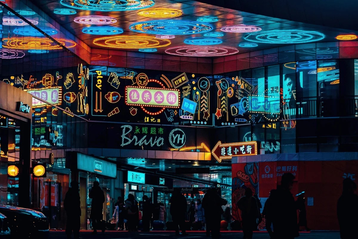 Vibrant neon-lit city street with reflections on mirrored surfaces at night.